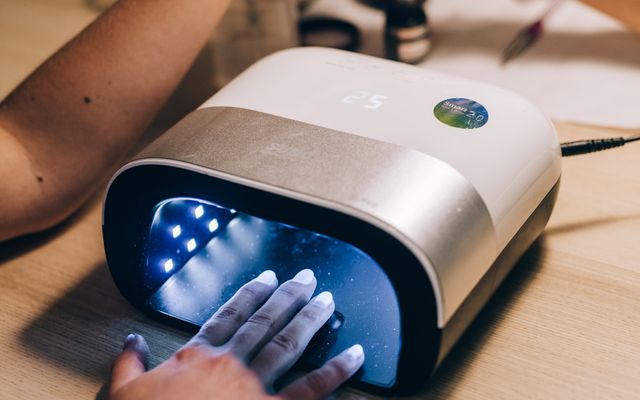 Hand curing gel nails inside a white and silver nail lamp with a lit timer on its top