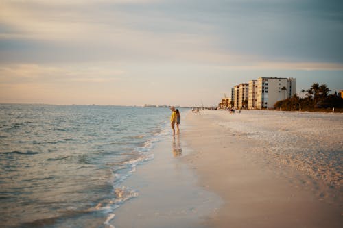 Anonymous couple standing on sandy seashore at sundown