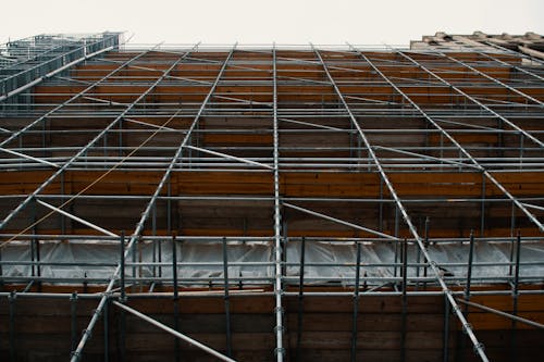 Low angle view of metal scaffolding standing near repairing building against cloudy sky