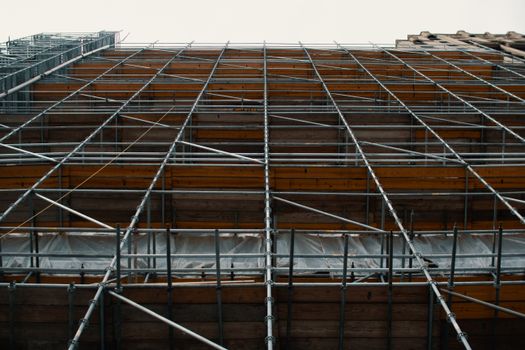 Low angle view of metal scaffolding standing near repairing building against cloudy sky