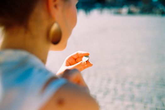 一名女子在户外场景中，从肩部拍摄，手持一枚硬币