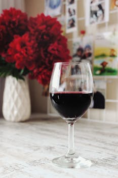 一杯优雅的红酒，配上瓶中鲜艳的红花，营造出温馨的室内氛围