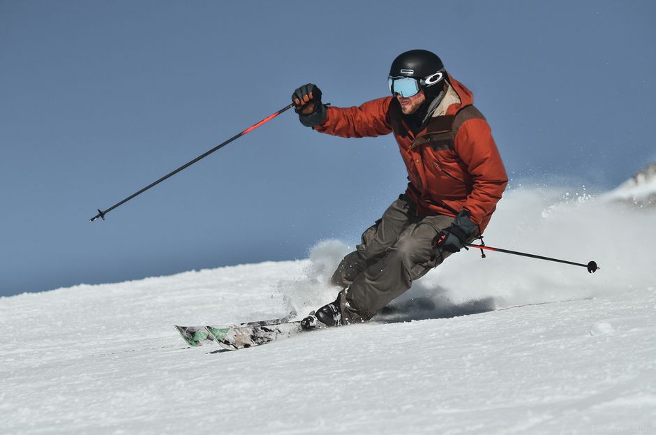 A skier in winter clothing races downhill on a snowy slope under clear skies.