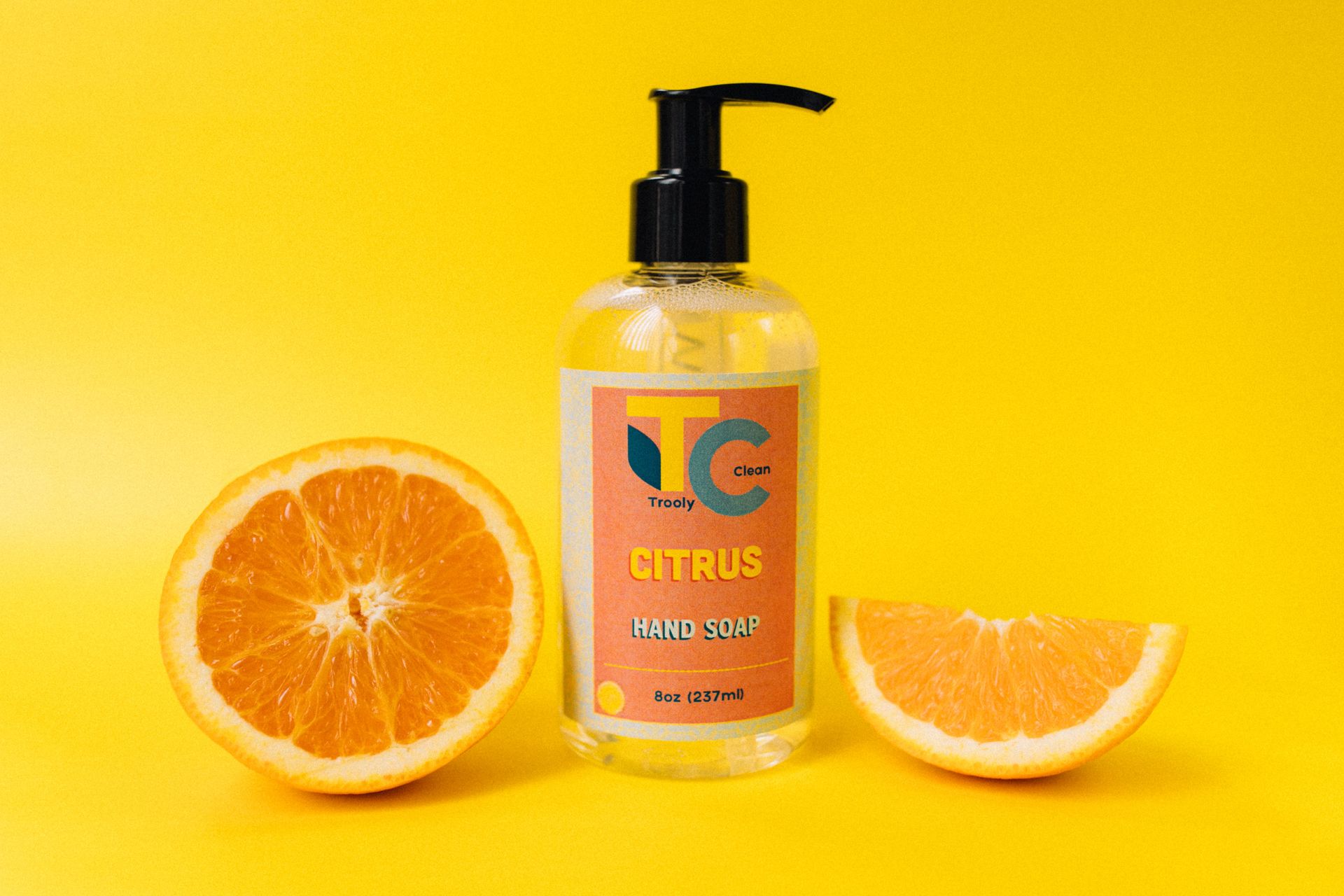 Colorful citrus hand soap bottle with fresh orange slices against a bright yellow background.