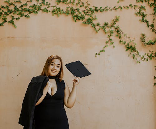 Cheerful woman with graduation cap in hand