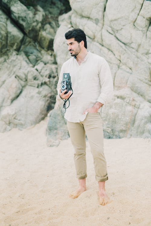 Photo of a Man Holding a Camera while Standing on Brown Sand