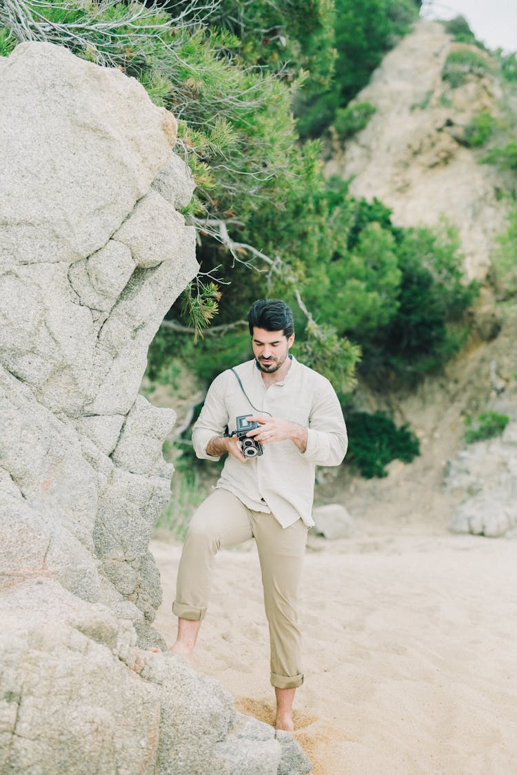 A Man Holding A Camera While Standing On A Rock