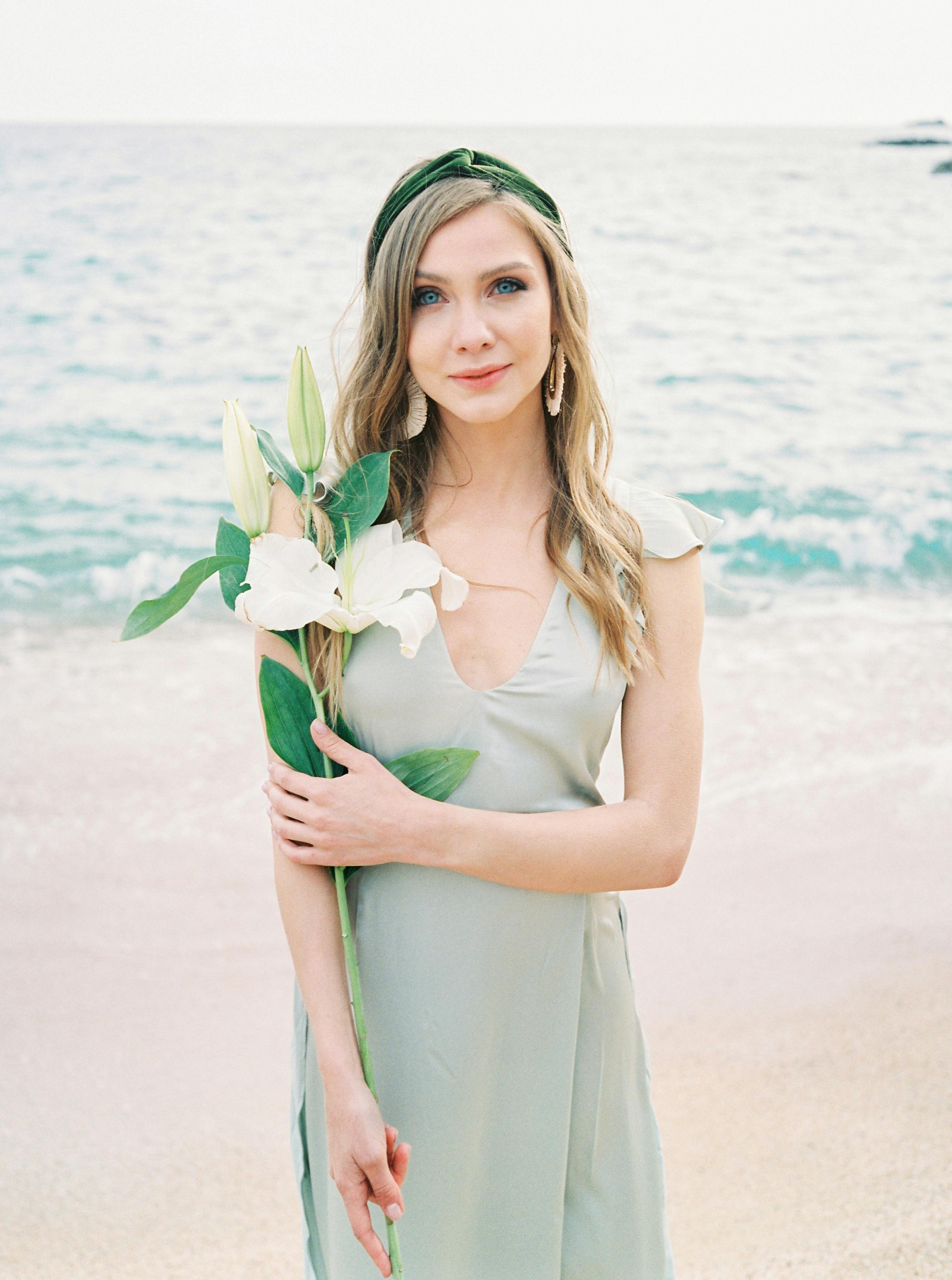 一位年轻女子身着连衣裙，手拿百合花，站在海滩边的肖像