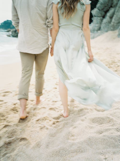 Man and Woman Holding Hands While Walking on Beach