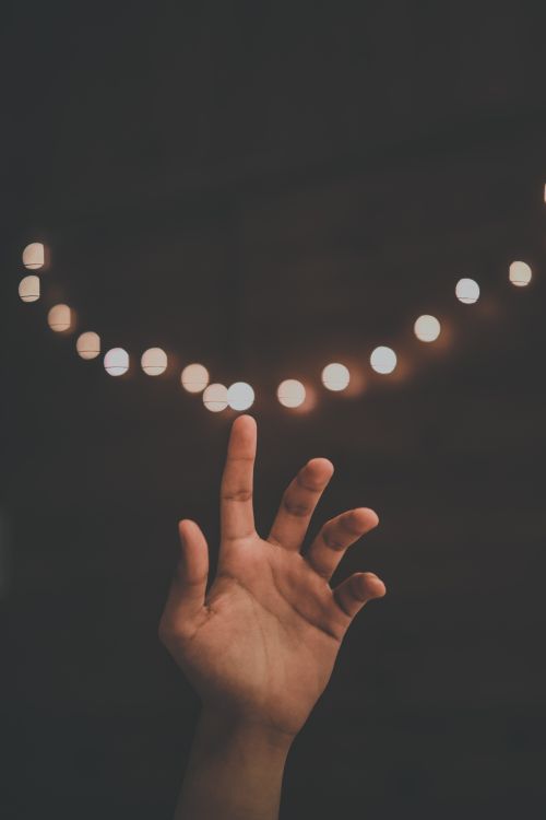 Free A hand reaching towards out-of-focus string lights, creating a dreamy atmosphere. Stock Photo