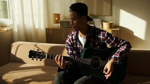 Man Sitting on Sofa Playing Guitar