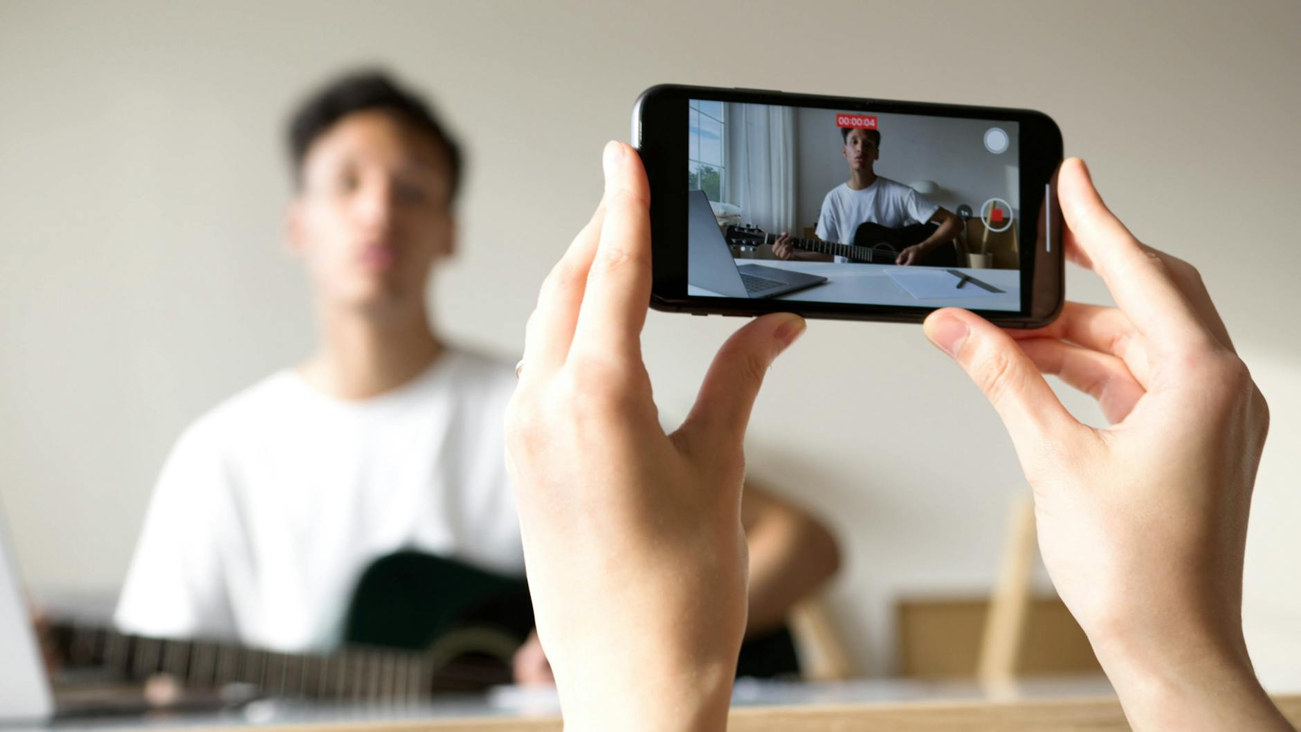 Person recording a guitar video indoors using a smartphone, showcasing online vlogging.