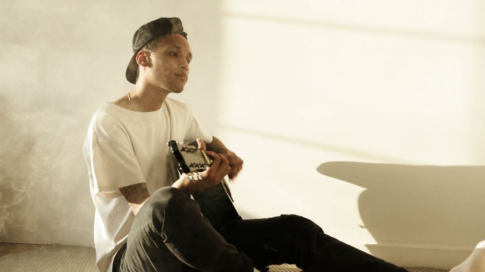 A young man playing guitar in a sunlit room