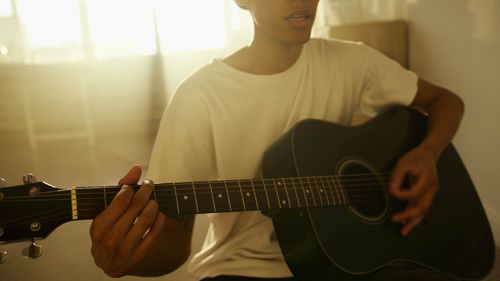 Free A man strumming a guitar indoors with warm sunlight filtering through a window. Stock Photo