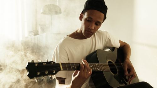 Free A young musician strums an acoustic guitar indoors, surrounded by a smoky atmosphere. Stock Photo