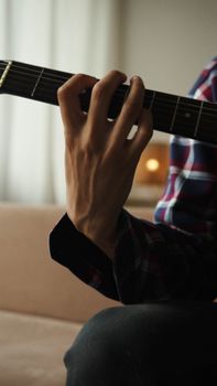 Detailed close-up of a musician's hand playing chords on an acoustic guitar indoors.