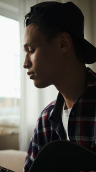 Portrait of a young man playing a guitar indoors with a serene expression.