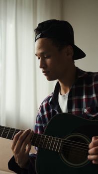 Young man in plaid shirt playing an acoustic guitar indoors. Captures musical focus.