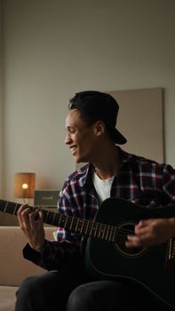 Smiling young man strumming an acoustic guitar indoors in a relaxed setting.
