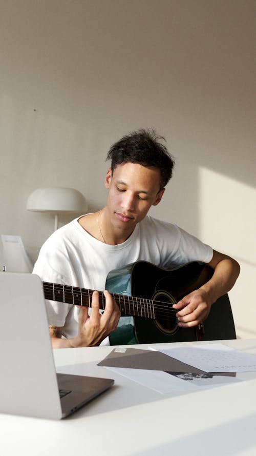 Man Playing a Guitar In Front of a Laptop