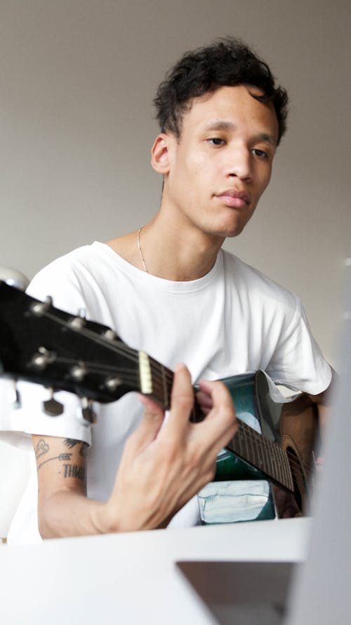 Man Looking at a Laptop While Playing a Guitar