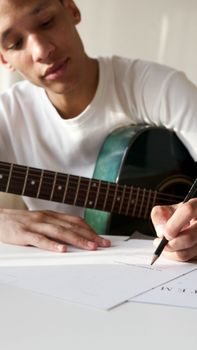 Man writing music notes with a guitar on a table, focused and creative scene.