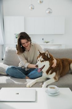 一位年轻女子和她的西伯利亚哈士奇犬一起躺在现代客厅的沙发上放松