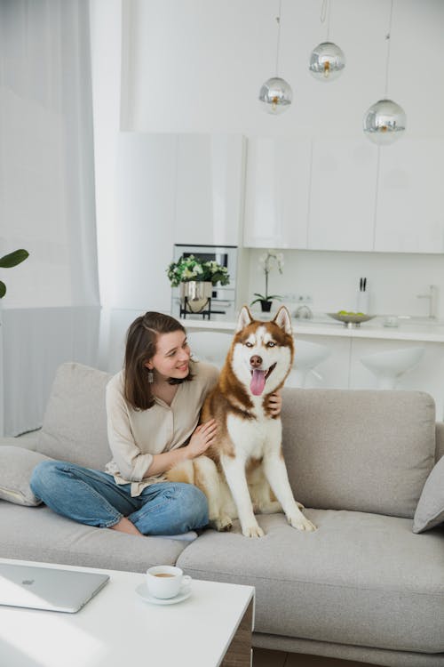 A Woman Sitting on a Sofa Hugging her Dog 
