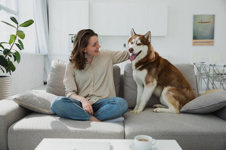 A Woman Sitting On A Couch Posing With Her Dog