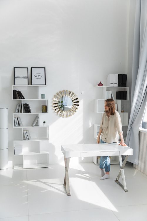 Free Bright home office with white decor and a woman standing by a desk. Stock Photo