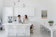 一对夫妇在明亮洁白的厨房里聊天，旁边有一只哈士奇