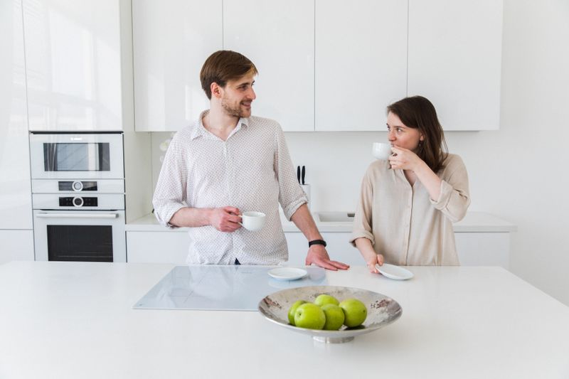 Couple enjoying coffee in a modern white kitchen setting with a stylish interior.