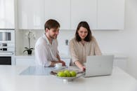 一对夫妇在现代化的白色厨房里边喝早晨的咖啡边用笔记本电脑