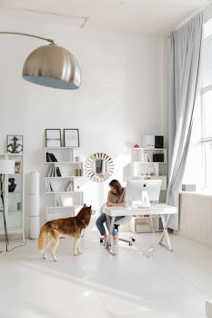 A woman working in a stylish home office with a dog next to her, surrounded by shelves and decor.