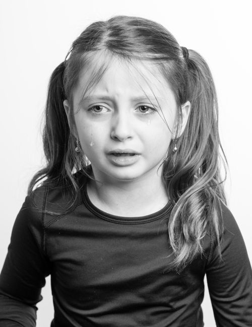 Free Black and white young girl with hair up in casual clothes crying against white background Stock Photo