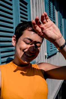 Cheerful woman in vibrant yellow tank top enjoying sunlight with hand shielding her eyes.