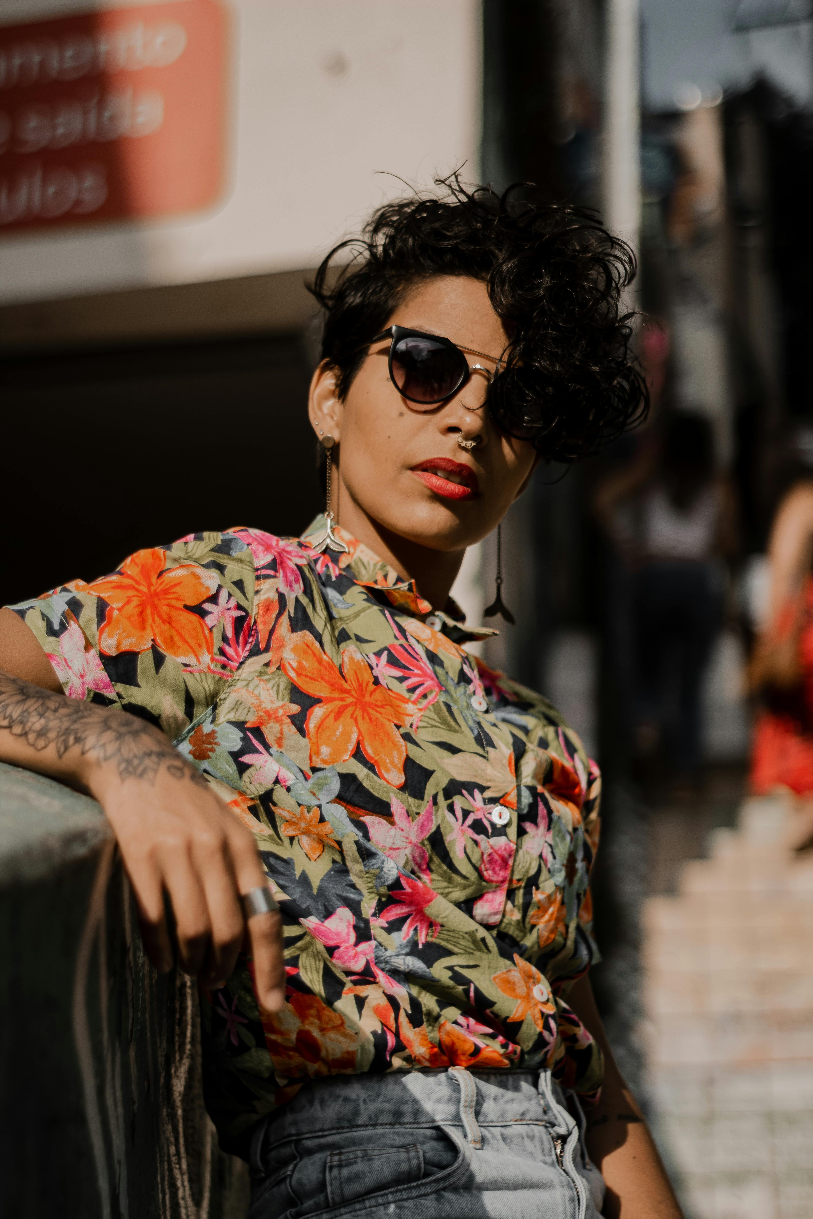 Confident woman wearing a floral shirt and sunglasses on a sunny day, showcasing style and individuality.