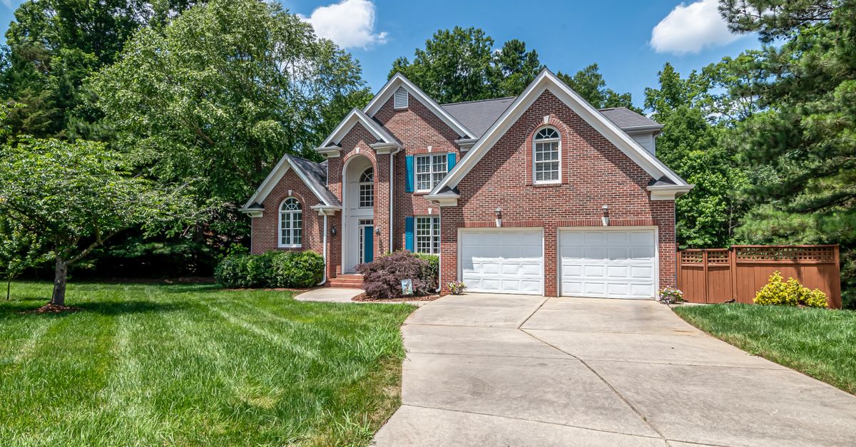 Beautiful brick house with double garage and lush green surroundings under a clear blue sky.