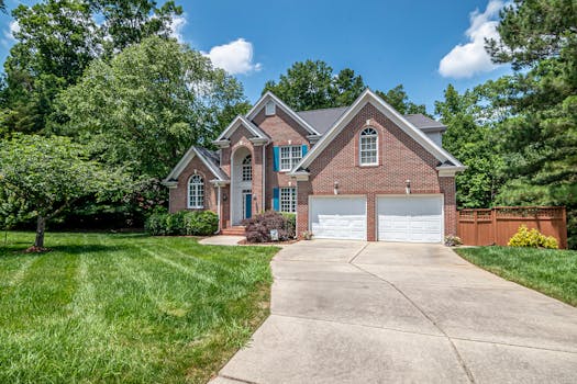 Beautiful brick house with double garage and lush green surroundings under a clear blue sky.