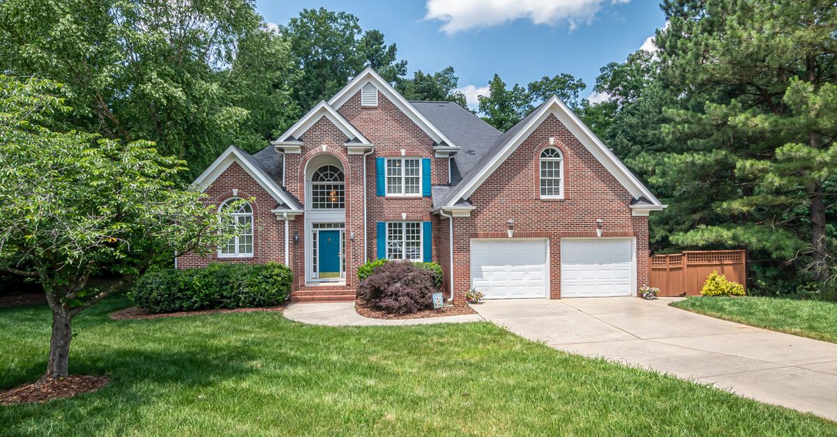 Charming two-story brick house with lush lawn and vibrant trees.