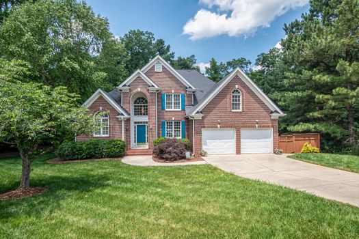 Charming two-story brick house with lush lawn and vibrant trees.