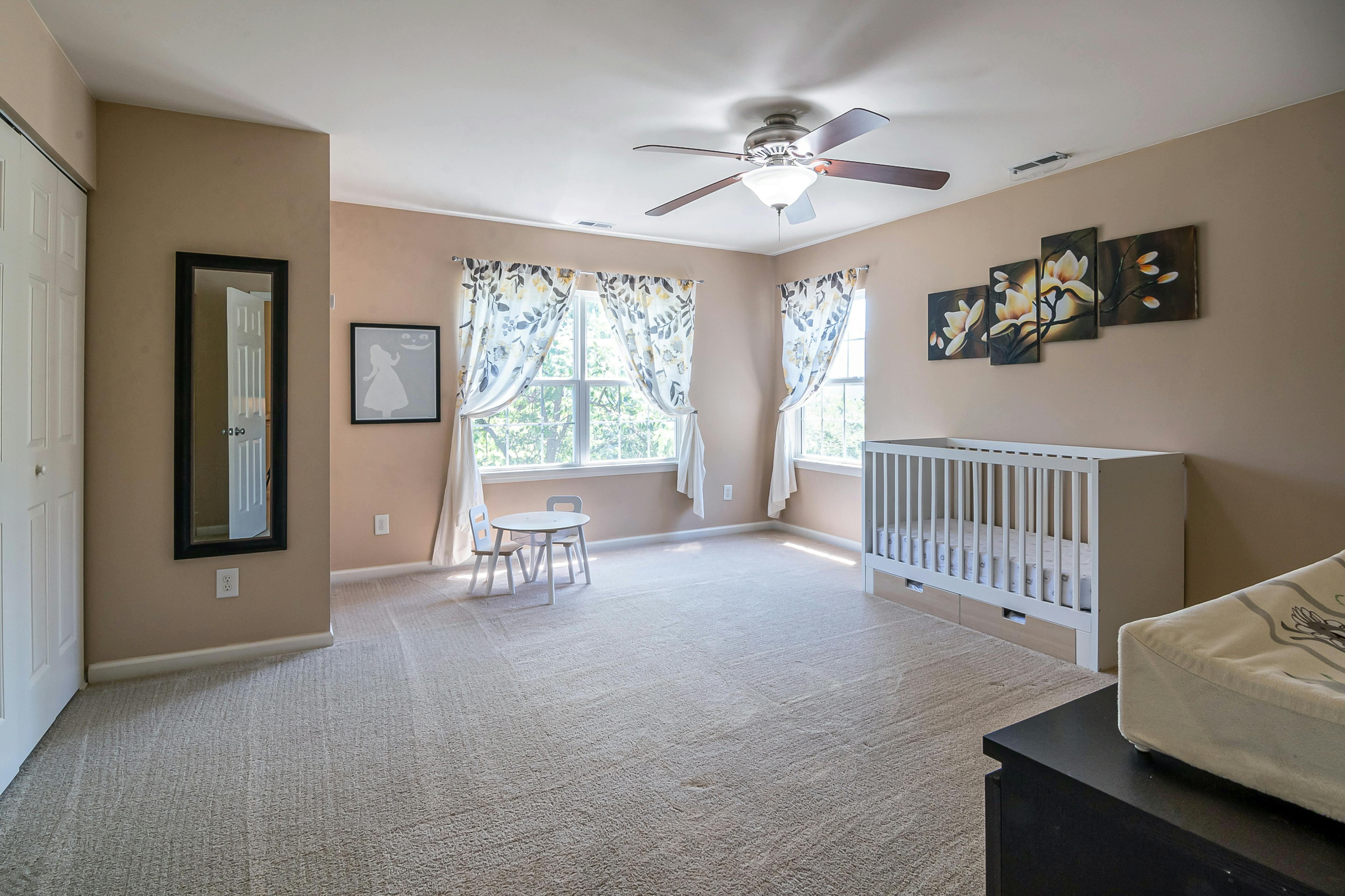 Spacious nursery room featuring a crib, decor elements, and soft carpeting in a serene setting.