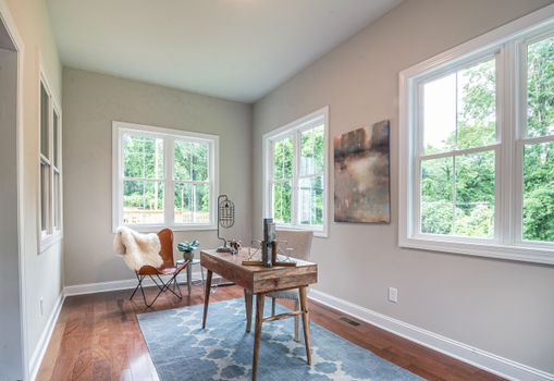 A sunny home office featuring modern furniture, decor, and abundant natural light from large windows.