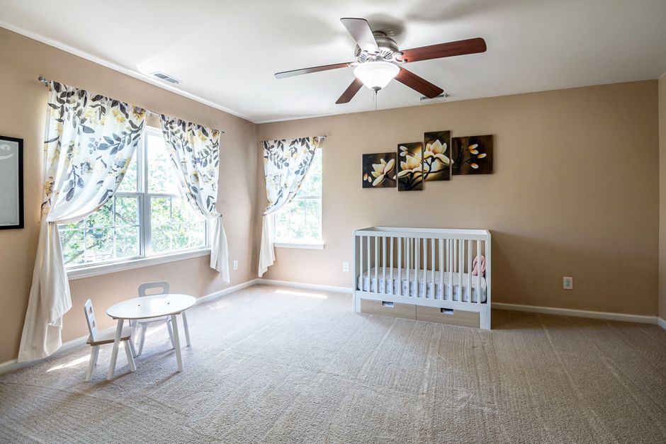 What Safety Research Reveals About Cribs, Monitors, and Sleep Gear A spacious nursery room with a crib, white table and chair set, and floral curtains under natural light.
