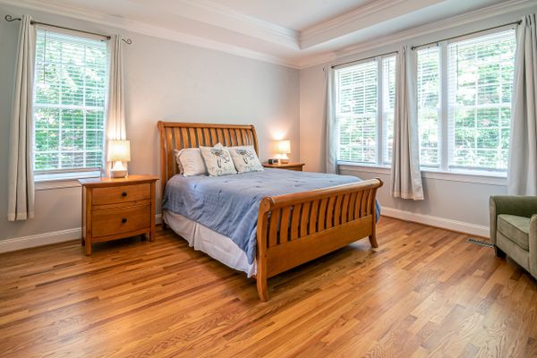 Bright guest bedroom with a wooden bed frame and tall windows — photo by Curtis Adams on Pexels