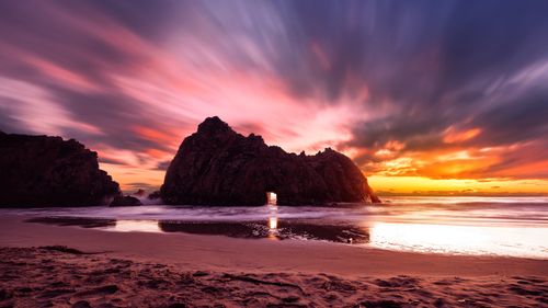 Free Breathtaking view of a sunset over a rock formation by the ocean shore with vibrant skies. Stock Photo