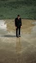 Melancholic man in suit standing on wet ground in park