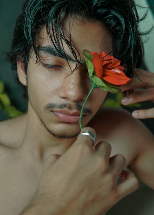 Young ethnic calm man with red flower