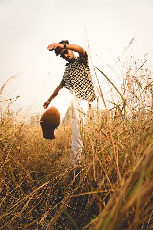 Low angle full body of young guy kicking dry grass while walking in meadow