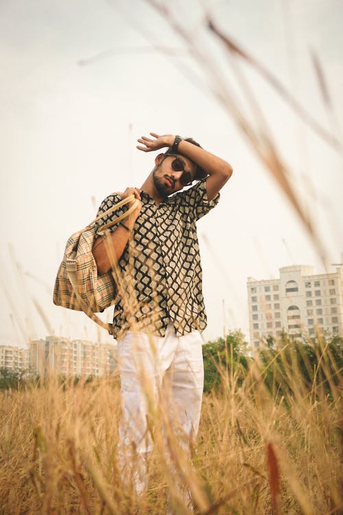 Stylish confident man with bag in dry meadow